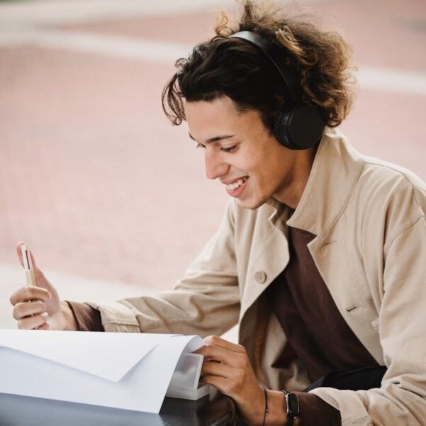Smiling student smiling happily while preparing homework project while listening to music in wireless headphones