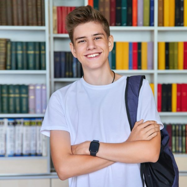 Single portrait of smiling confident male student teenager looking at camera in library